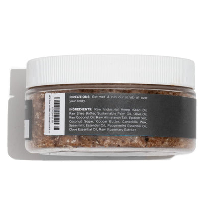 A clear plastic jar with white ribbed lid contains brown granular body scrub stay ready scrub with ingredient label