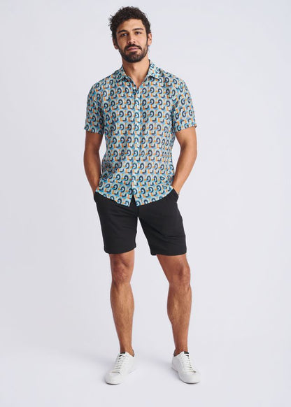 A man wearing a swirls lightweight cotton silk short-sleeved shirt with blue teal and beige circular patterns