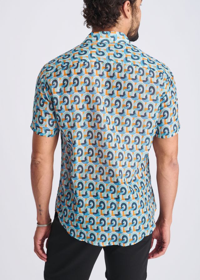 A man wearing a swirls lightweight cotton silk short-sleeved shirt with blue and orange geometric patterns on turquoise