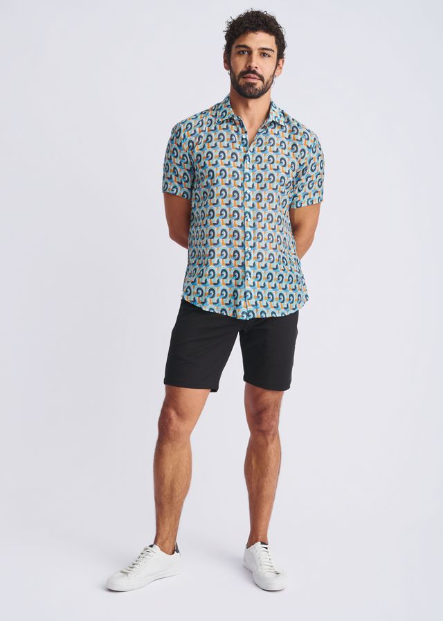 A man wearing a swirls lightweight cotton silk short sleeve shirt with blue green and yellow circular patterns on light teal