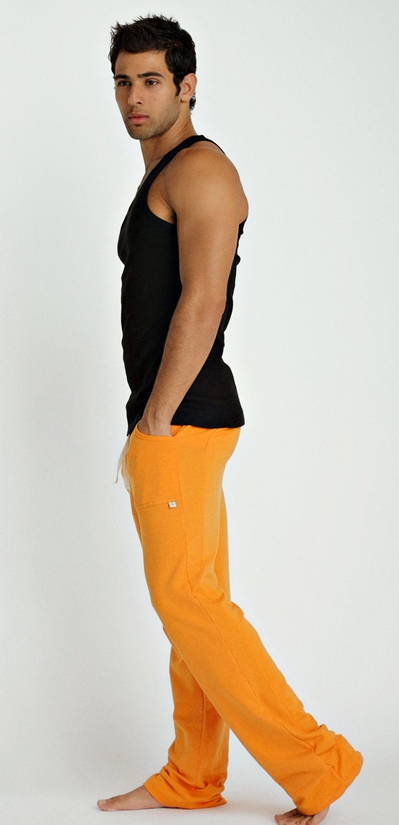 Bright orange loose-fitting pants with small white logo on thigh paired with sustain tank top black