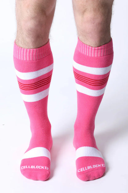 Bright pink tight end knee high socks with white and red stripes featuring cellblock13 logo on the toe
