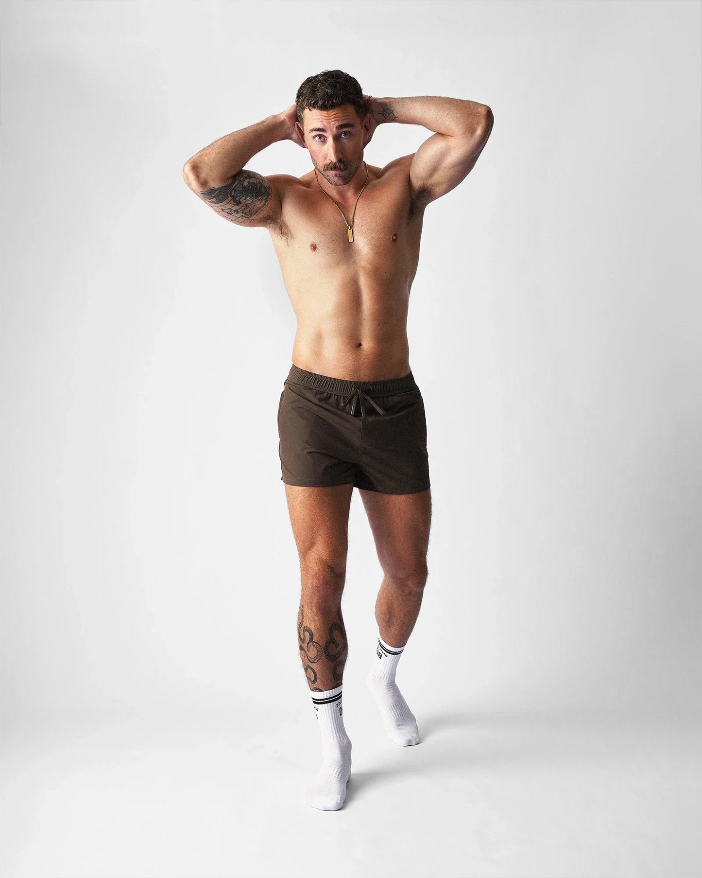 A person wearing brown Teamm8 Bolt 3-inch gym shorts and white socks against a plain background.
