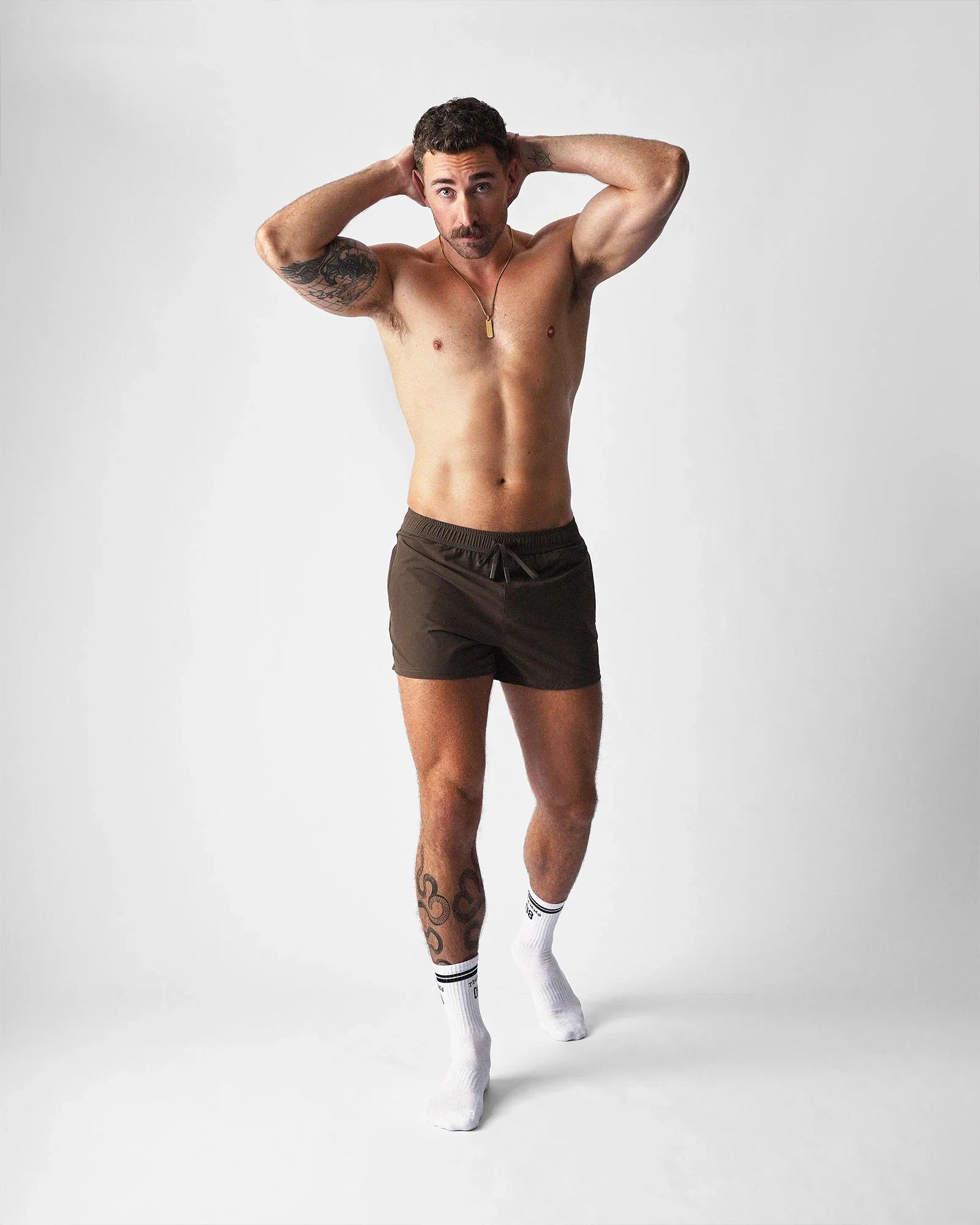 A person wearing brown Teamm8 Bolt 3-inch gym shorts and white socks against a plain background.