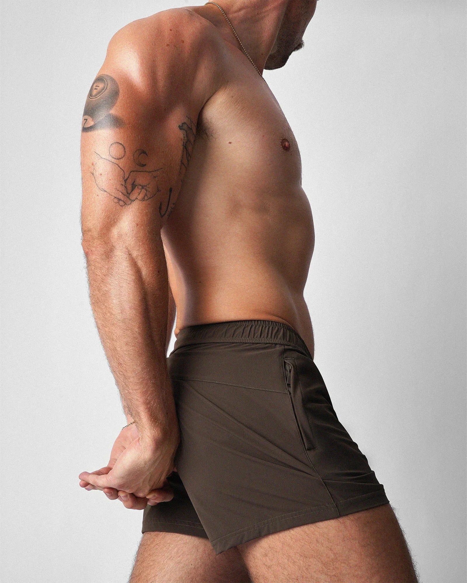 Side profile of dark brown athletic shorts with an elastic waistband and zippered side pockets.
