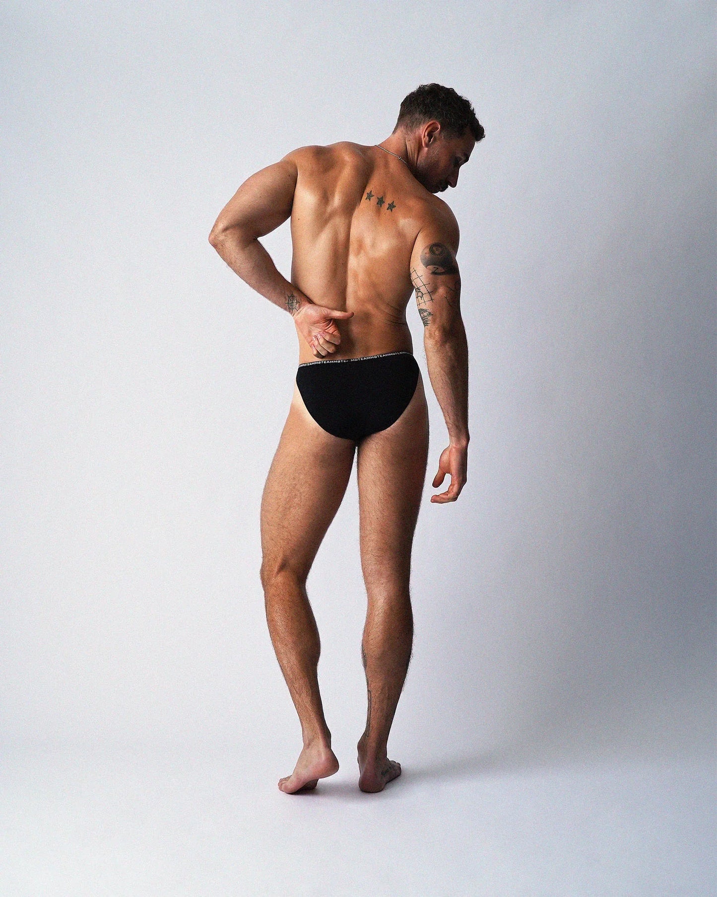 Rear view of a person wearing black teamm8 Glide Micro Brief underwear against a plain background.