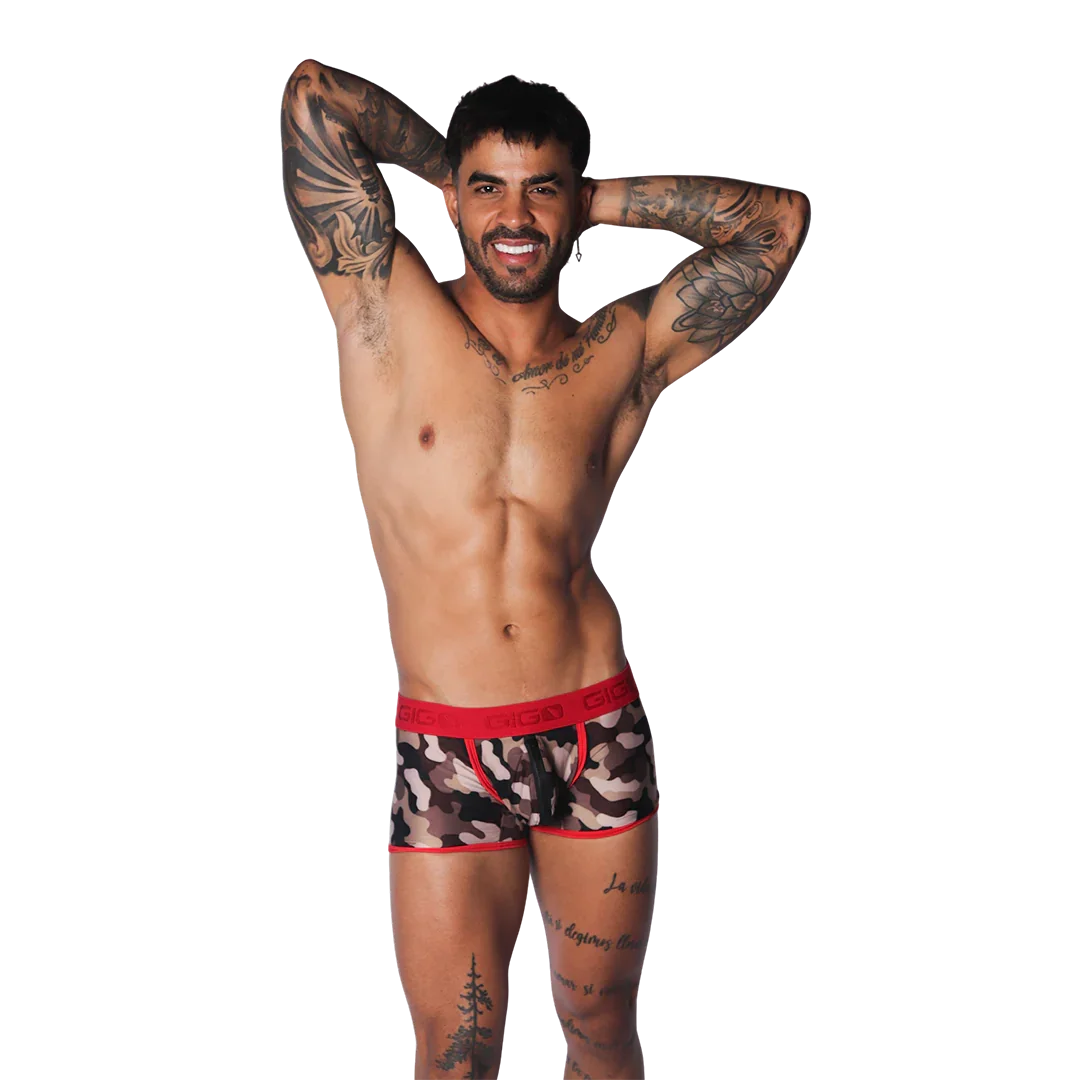 Camouflage print trunk with red trim and branded elastic waistband, worn by a tattooed model on a black background.