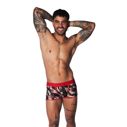 Camouflage print trunk with red trim and branded elastic waistband, worn by a tattooed model on a black background.
