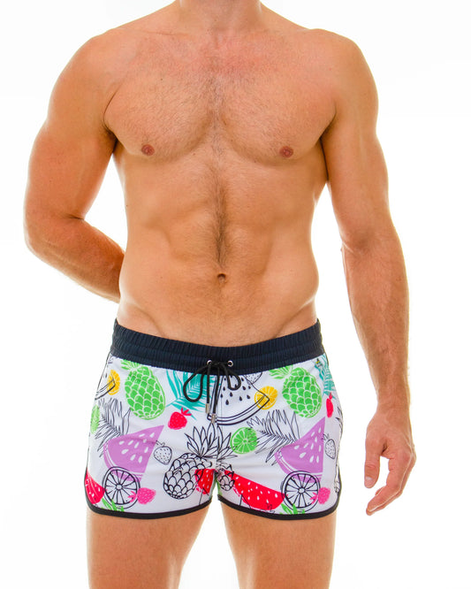White swim trunks with vibrant tropical fruit print featuring pineapples watermelons and strawberries in multiple colors
