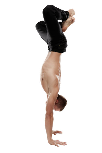 A shirtless man performing a handstand wearing black tactical urban at home dress pant yoga pants