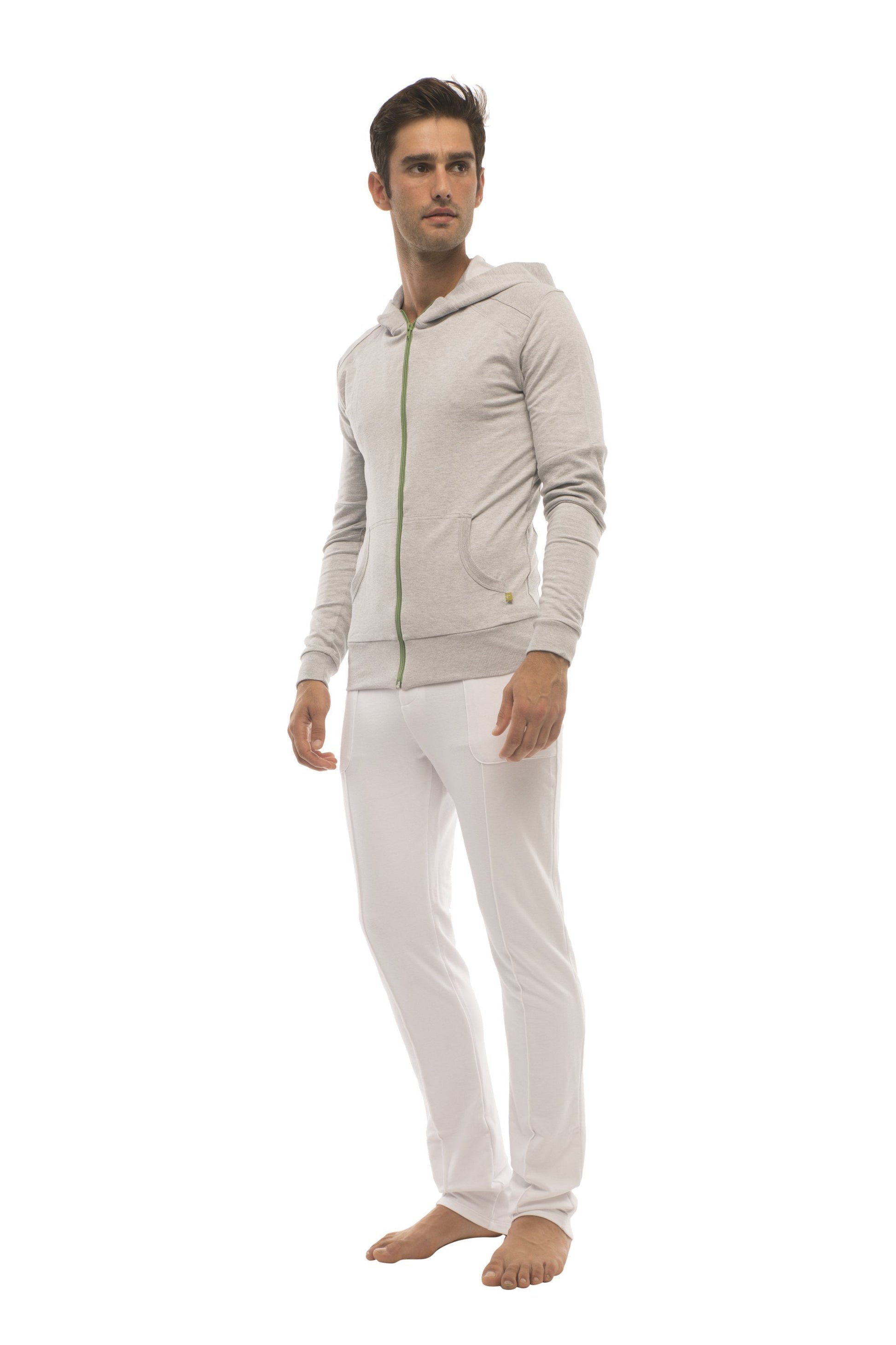 A man wearing a white tactical urban at home dress pant yoga pant paired with a light gray zip-up hoodie with green accents