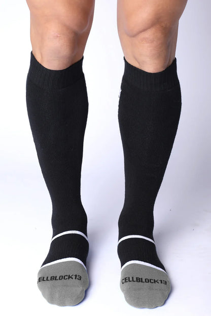 Front view of a person wearing black knee-high socks with grey toes and white stripes.