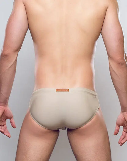 Beige form-fitting v10 core bikini swim trunks with a subtle orange brand tag at the waistband