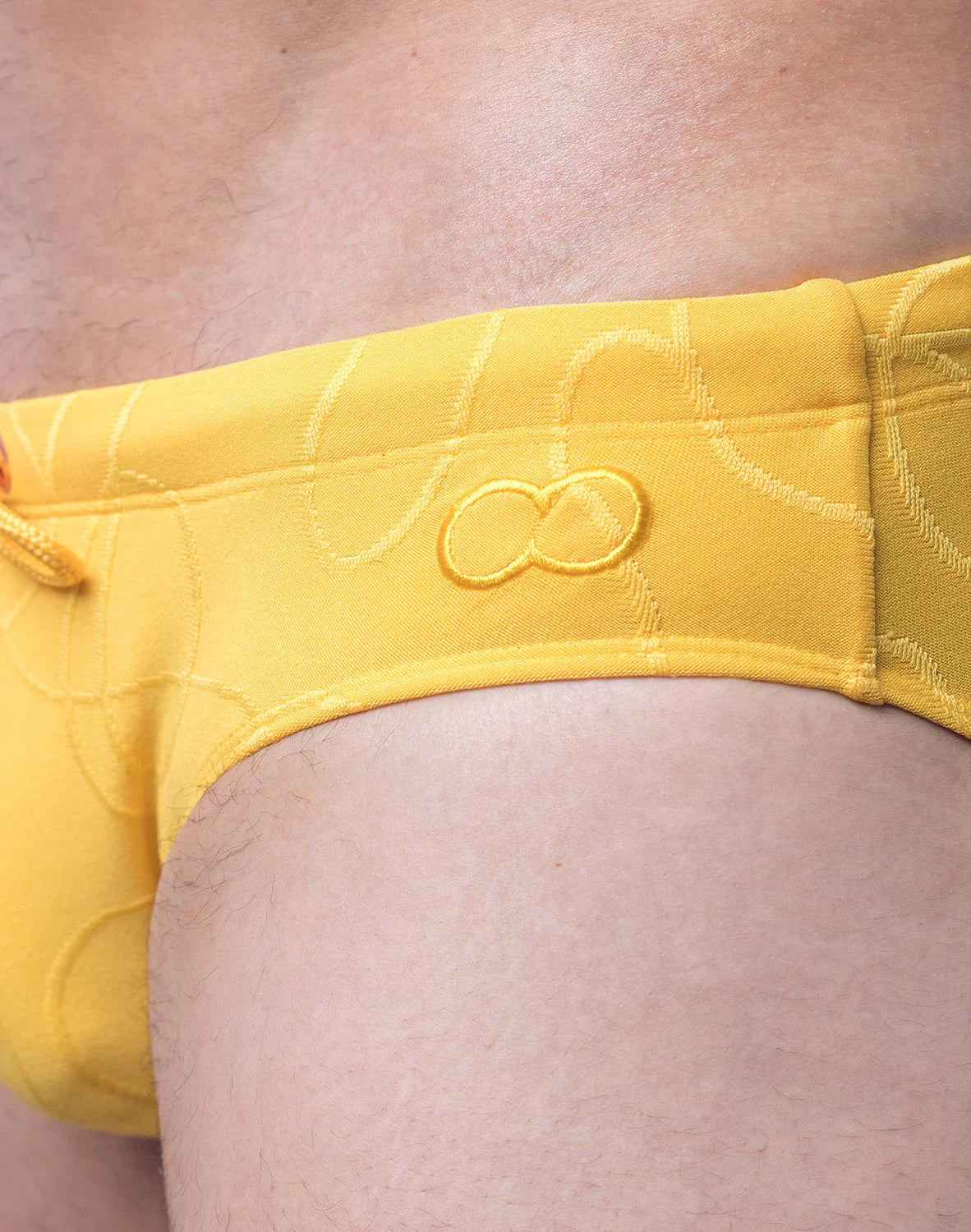 Bright yellow V10 ripple textured swim brief with subtle pattern and embroidered infinity symbol on the front