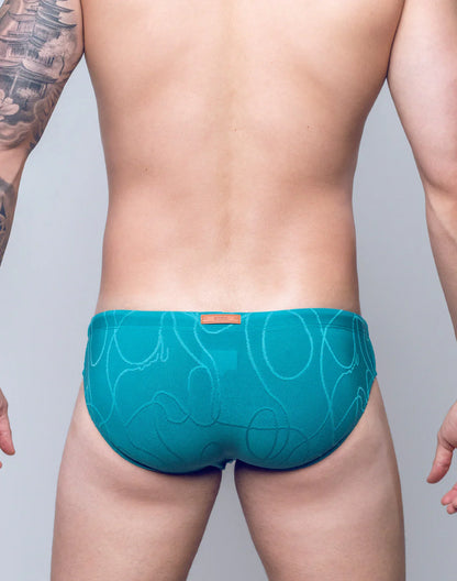 Teal v10 ripple textured swim brief with subtle abstract pattern and orange brand tag on the waistband