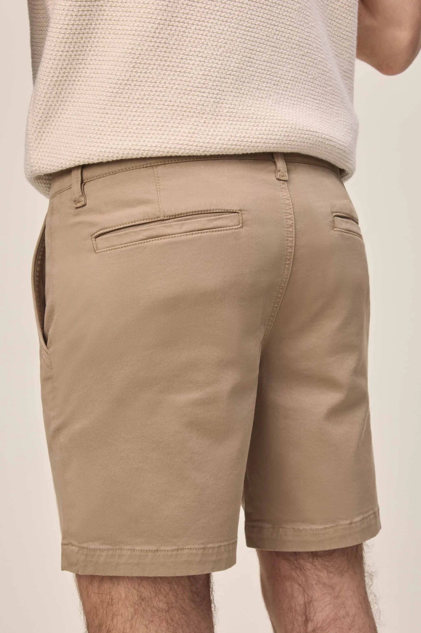 Rear view of tan chino shorts with welt pockets and belt loops, paired with a cream sweater.