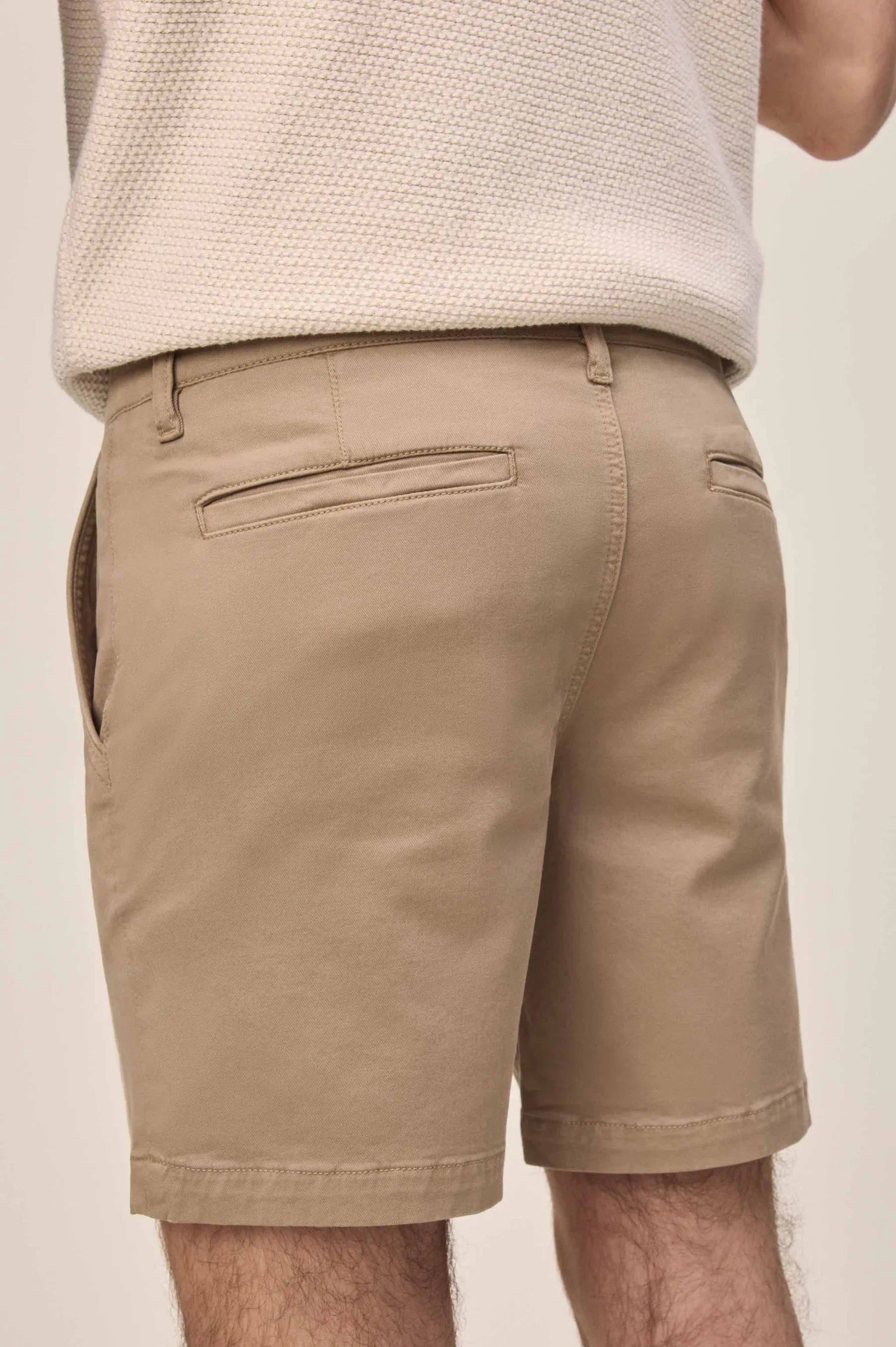 Rear view of tan chino shorts with welt pockets and belt loops, paired with a cream sweater.
