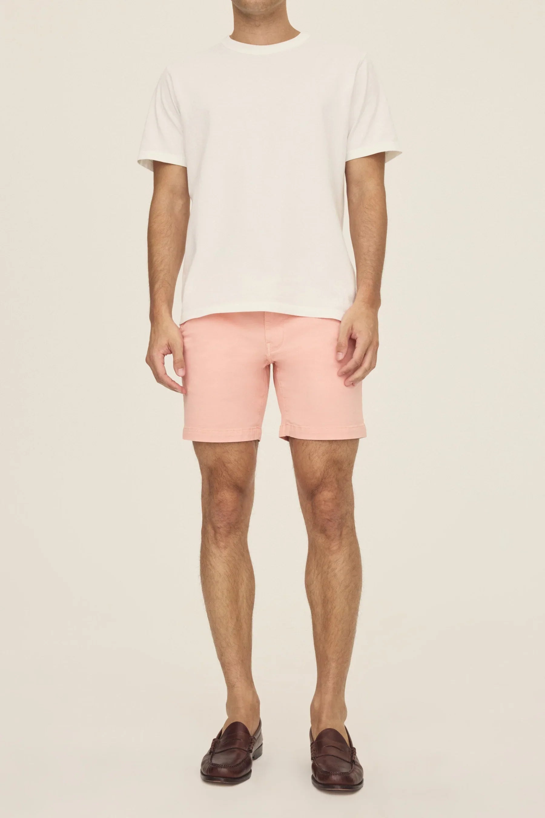 A person wearing a white t-shirt, pink chino shorts, and brown loafers.