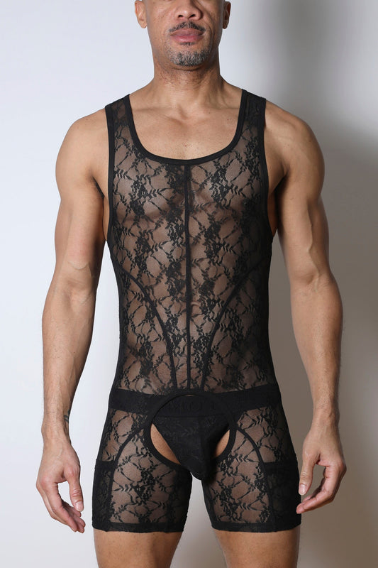 A person wearing a black lace singlet chaps with a low scoop neck and open-crotch design against a plain background.