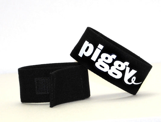 Black adjustable fabric cock ring with a velcro strap and white "piggy" text embroidery on a white background.