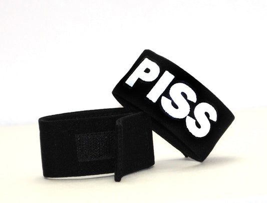 Two black fabric cock rings with velcro closures, featuring the word "PISS" in bold white lettering.
