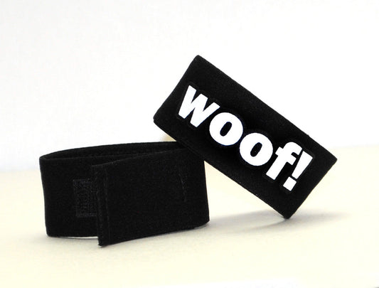 Black, adjustable fabric cock ring with white "WOOF!" lettering, featuring a velcro closure.