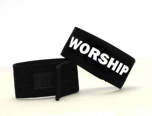 Two black fabric cock rings with adjustable velcro closures; one features the word "WORSHIP" in white bold letters.