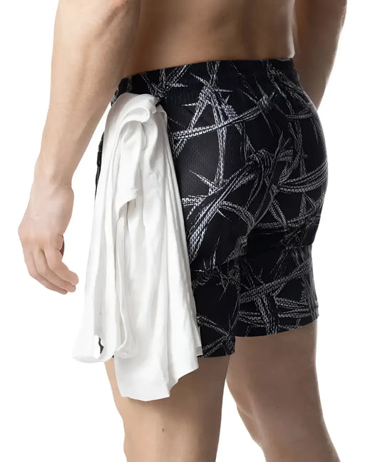 Black barbed wire rugby short swim trunks with bold white pattern and white towel tied around the waist
