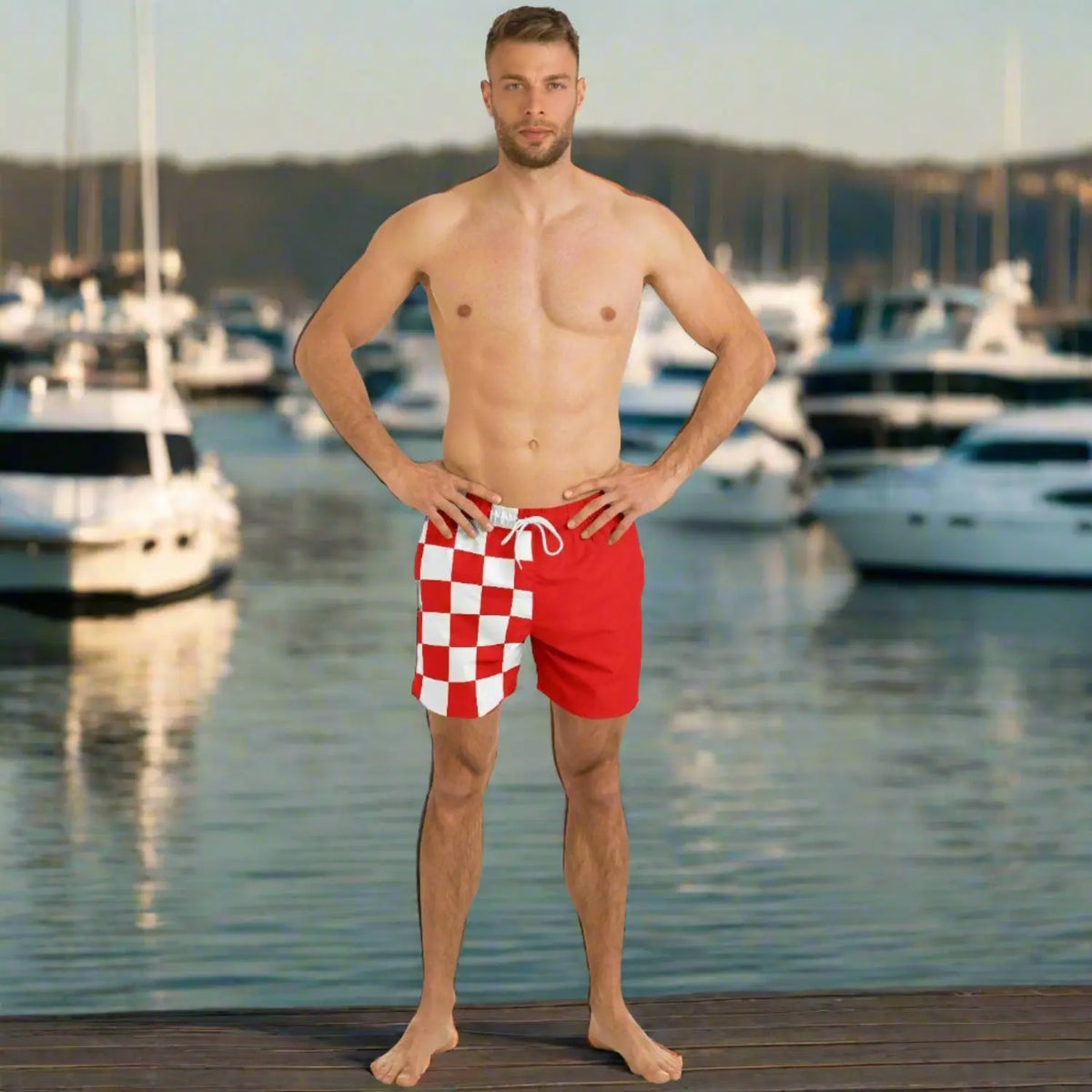 Men's red swim shorts with white checkered pattern made by Maris Equi shown on a model at a marina.