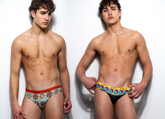 Two pairs of men's swim briefs by Maris Equi one with a colorful mosaic pattern and the other in solid black with a vibrant waistband.