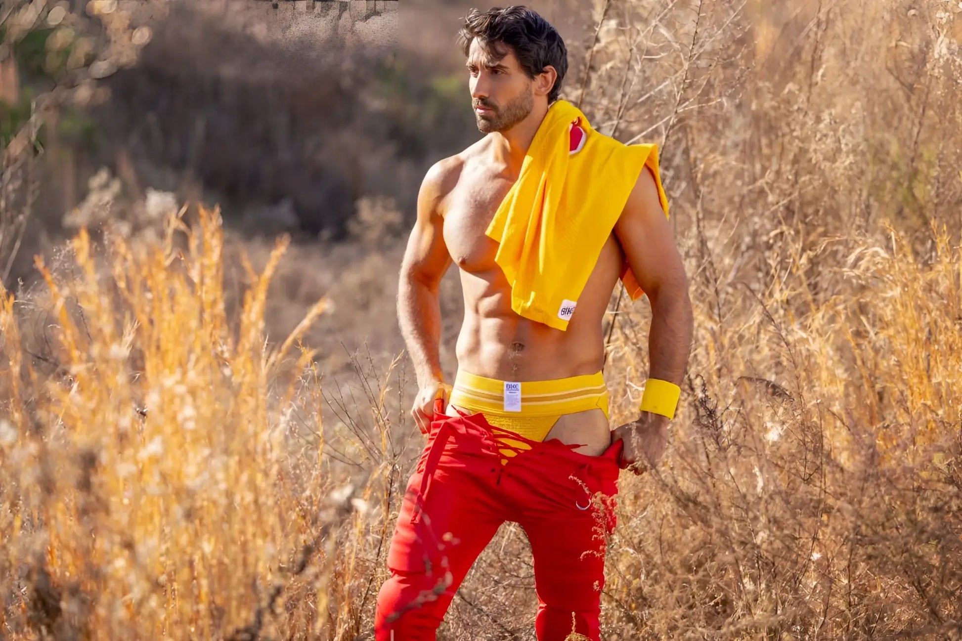 A man wearing bright red athletic pants with yellow trim and a yellow BIKE athletic jockstrap visible from the back side