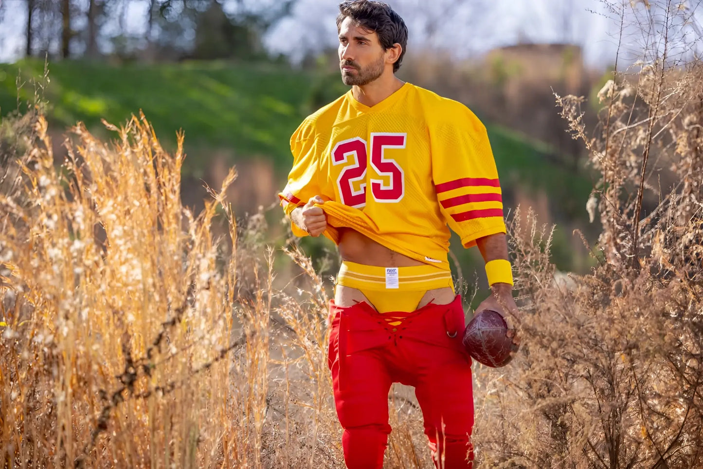 A man wearing a yellow jockstrap with a vibrant yellow and red football jersey and pants.