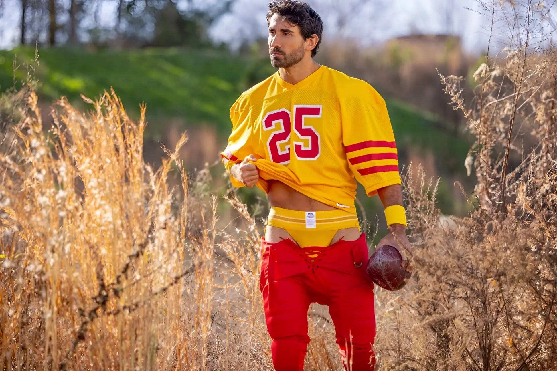 A man wearing a yellow jockstrap with a vibrant yellow and red football jersey and pants.