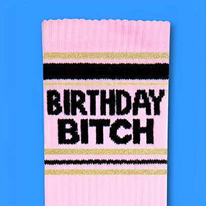 Pink knit birthday bitch crew socks with black and gold stripes featuring bold black lettering on the front