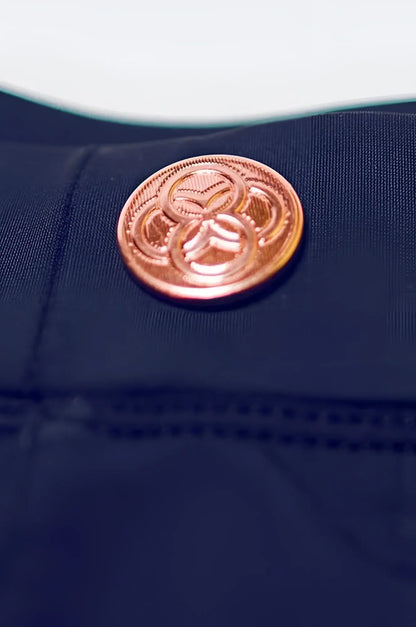 A copper-toned circular button with an intricate interlocking circle design on dark navy bondi short fabric