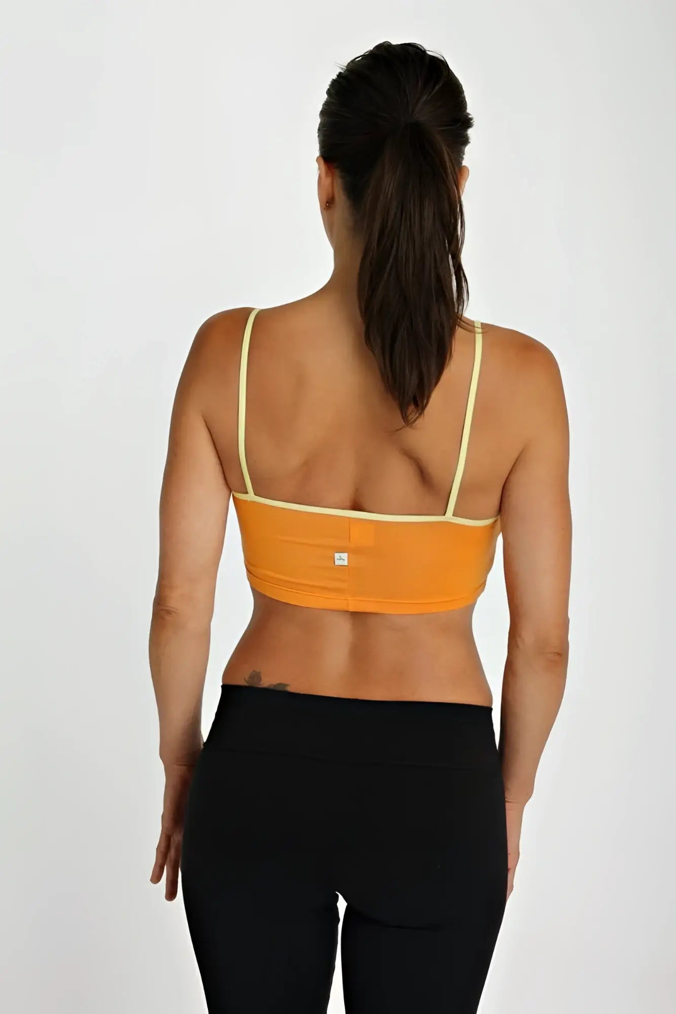 Back view of orange bra top tangerine with pale yellow straps and small white logo designed for activewear