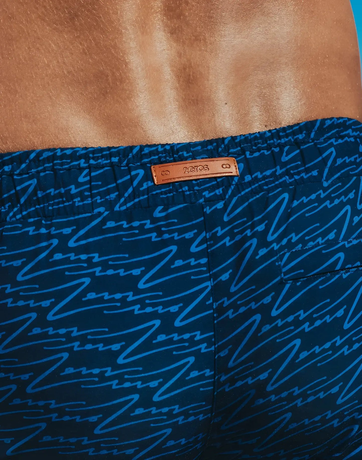 Dark blue Byron swim shorts with light blue abstract line print and tan leather brand tag for casual beachwear
