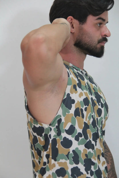 A man wearing a camouflage open arm tank with black green and tan splotches on a white base
