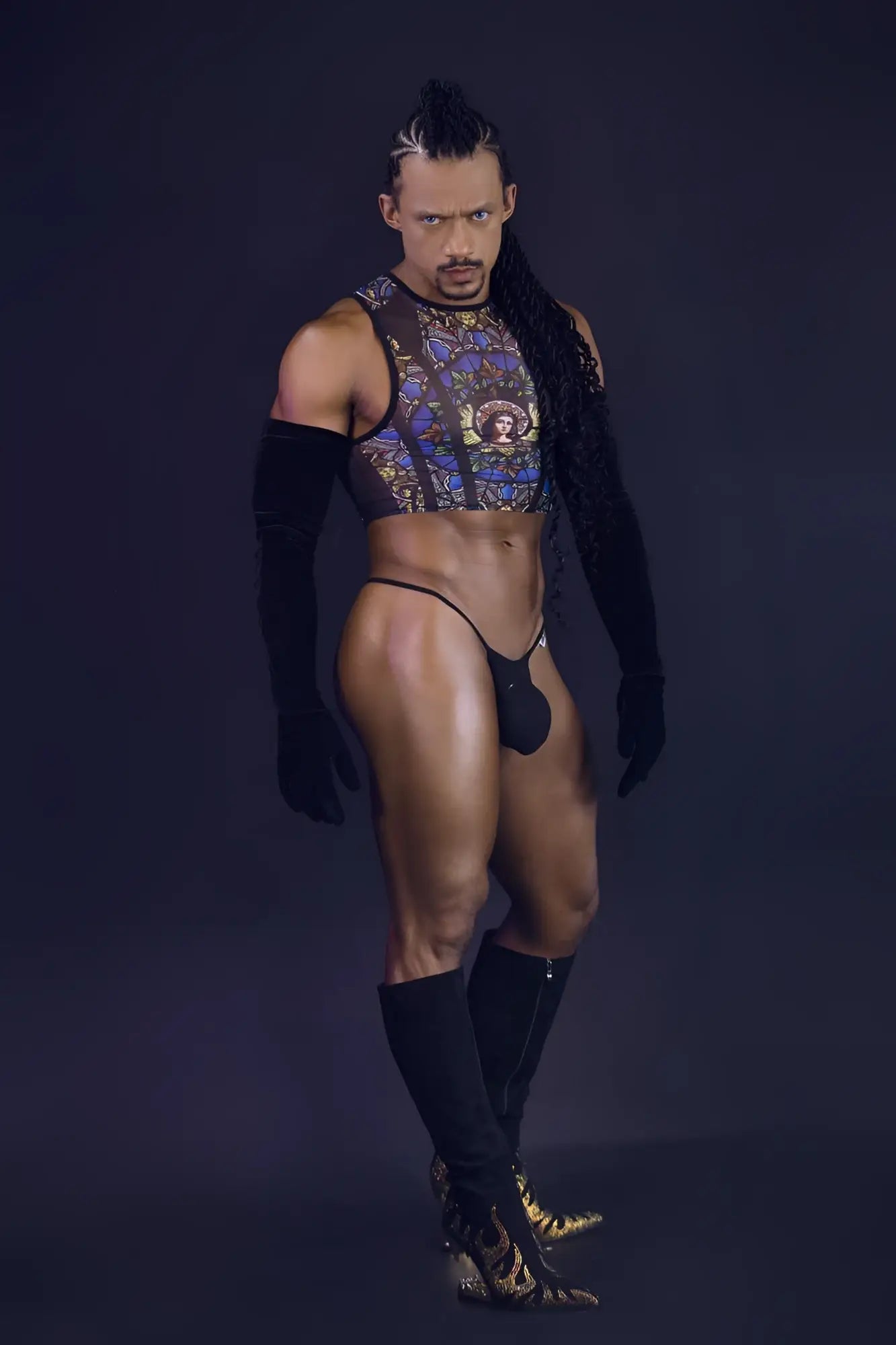 A man wearing a candyMan 99805 stained glass black print sheer patterned crop top with gold and blue designs