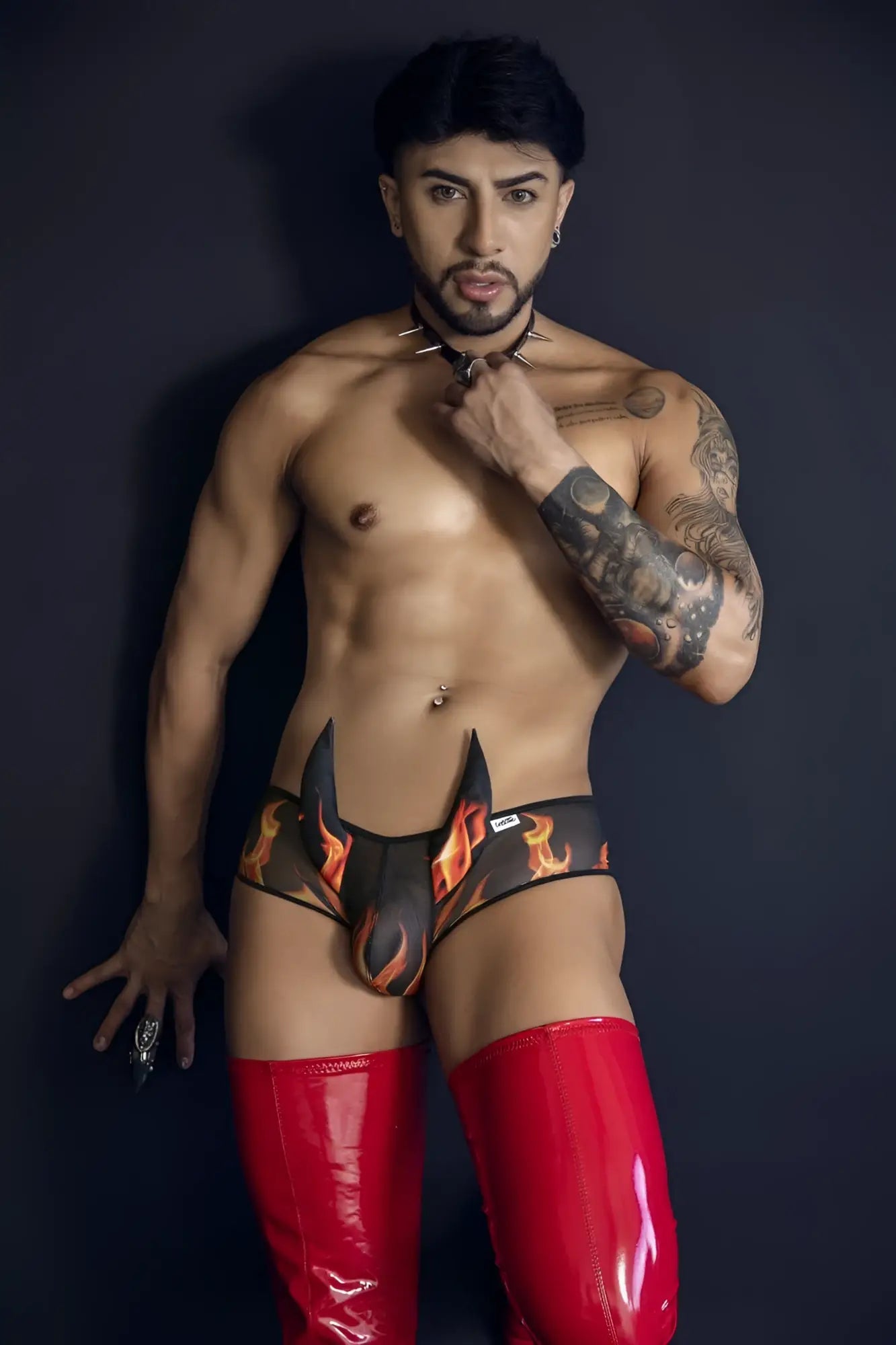 Black and orange flame-patterned CandyMan 99917 Wicked trunks briefs paired with glossy red latex thigh-high boot