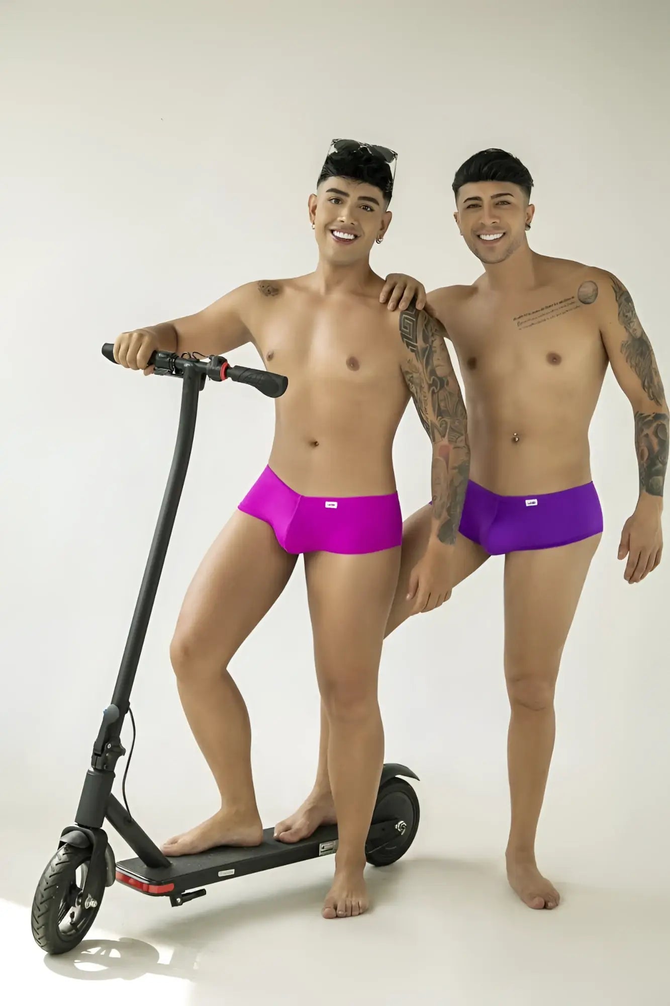 Two men wearing fitted magenta and purple CandyMan trunks with a sleek, minimalist cut.