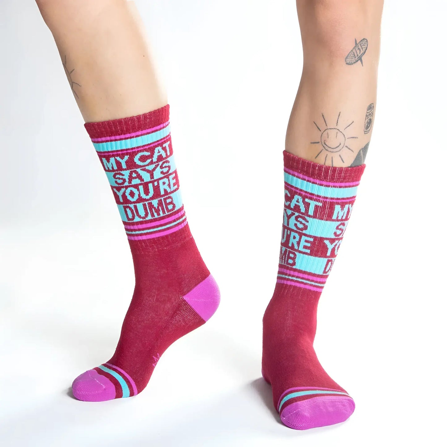 Maroon and pink crew socks with light blue band and white text saying my cat says youre dumb with thin stripes
