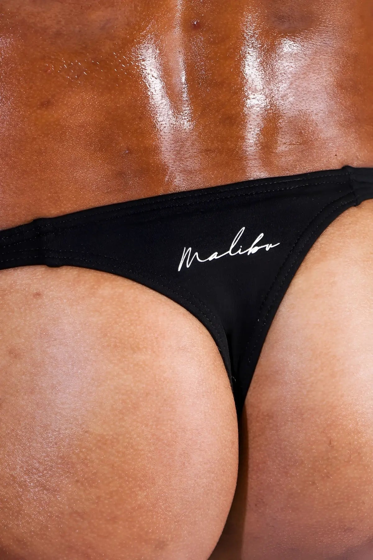 Black cheeky classic g-string thong with white cursive branding showing the front side in soft fabric