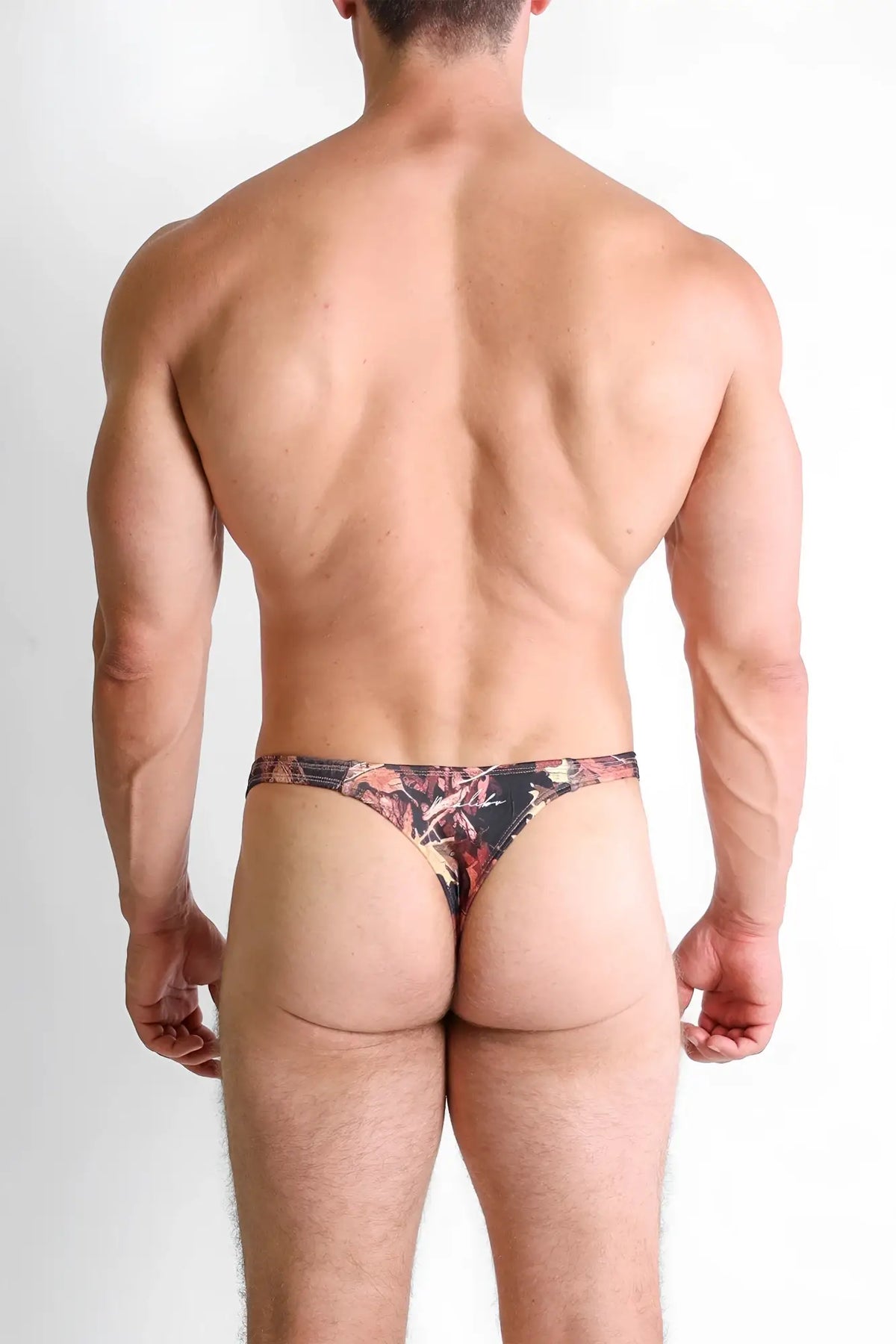 A man wearing the back side of a cheeky classic g-string thong in black red and brown leaf-patterned cajun camo