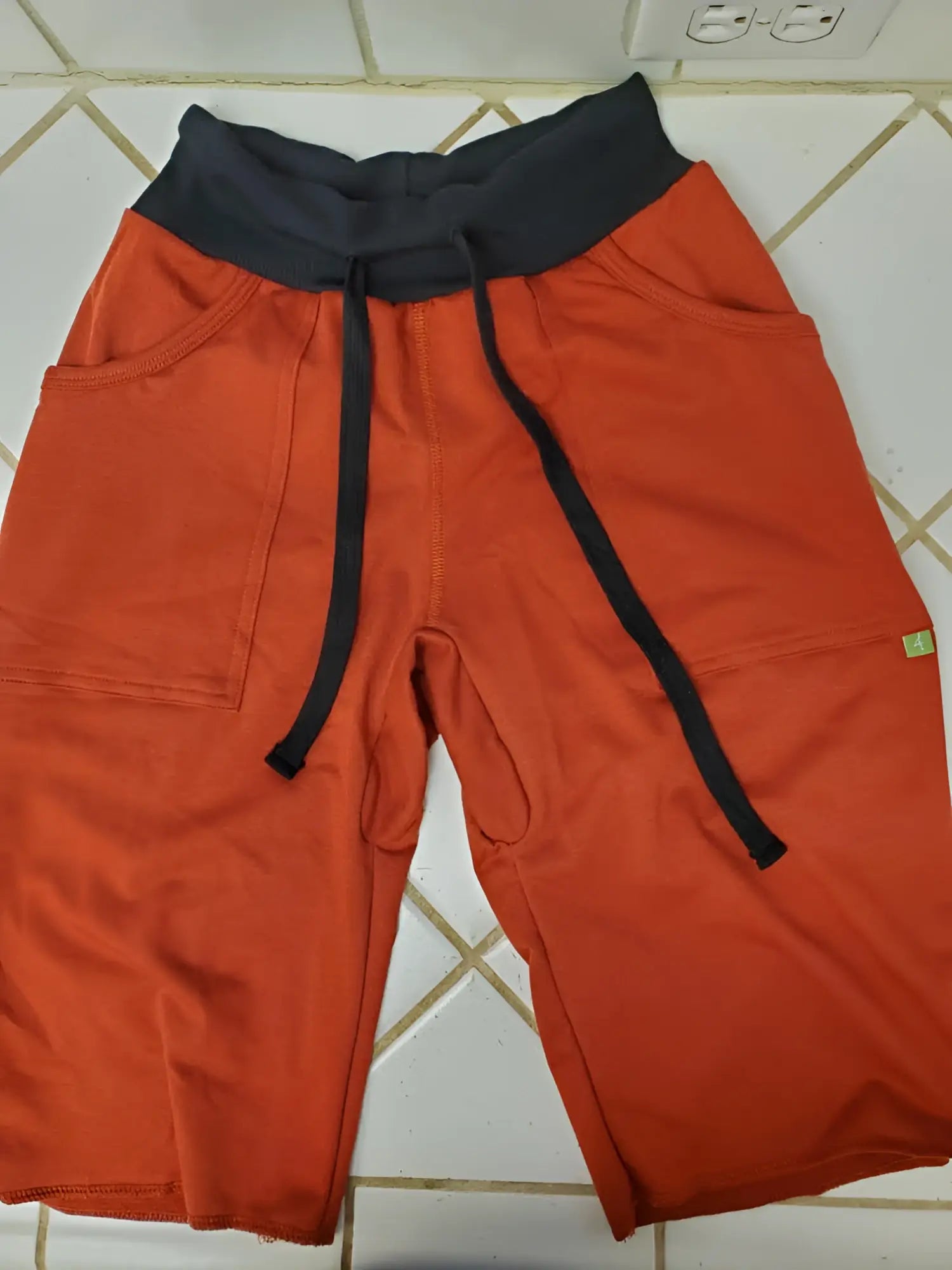 Eco-track short cinnabar orange athletic shorts with black elastic waistband drawstrings side pockets and green tag