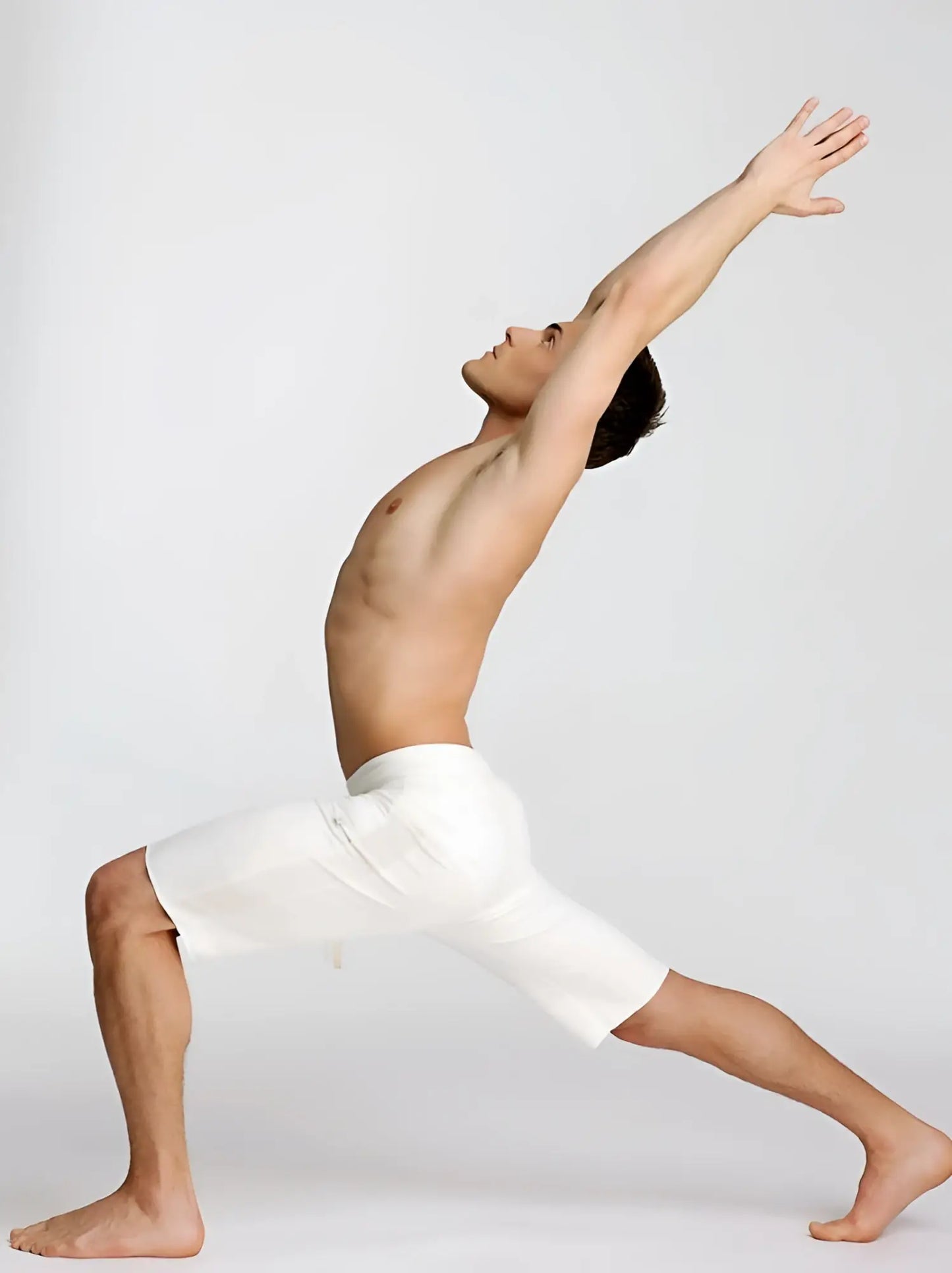 A man in white eco-track short yoga shorts performing a dynamic stretching pose showing the front view