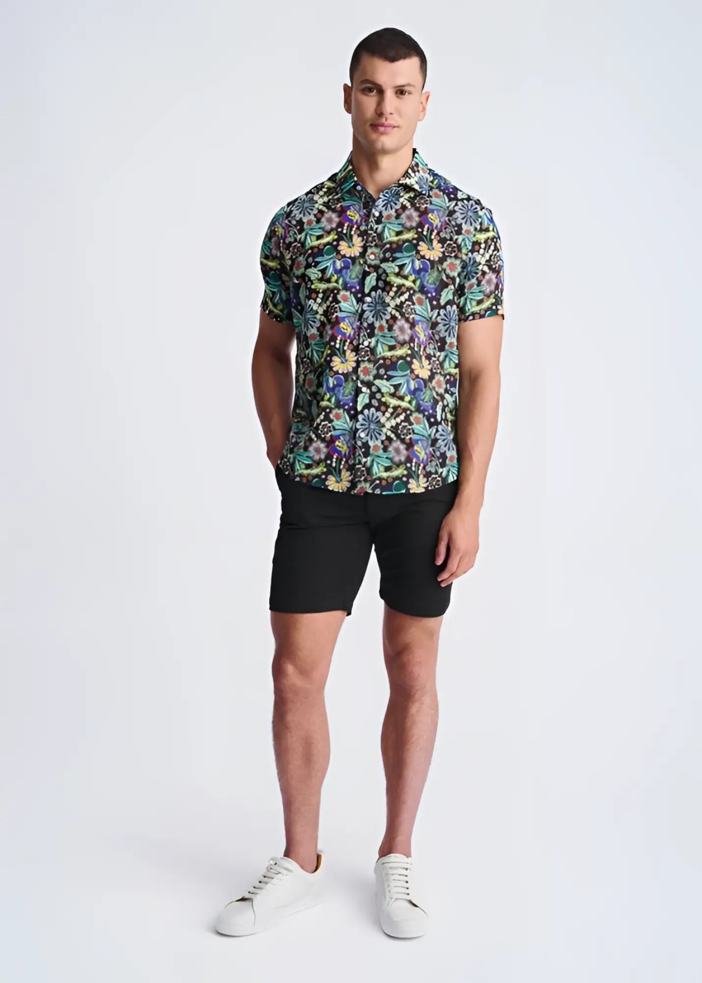 A man wearing a floral lightweight linen tencel short-sleeved shirt with multicolored pattern on a dark background