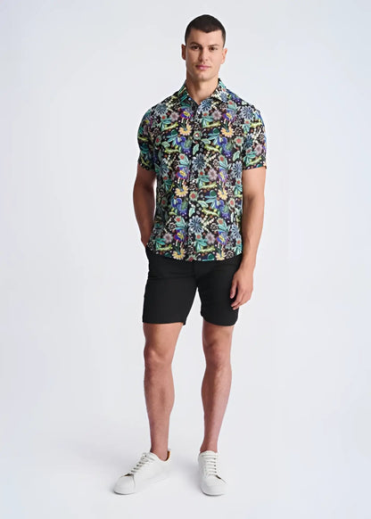 A man wearing a floral lightweight linen tencel short-sleeved shirt with multicolored pattern on a dark background