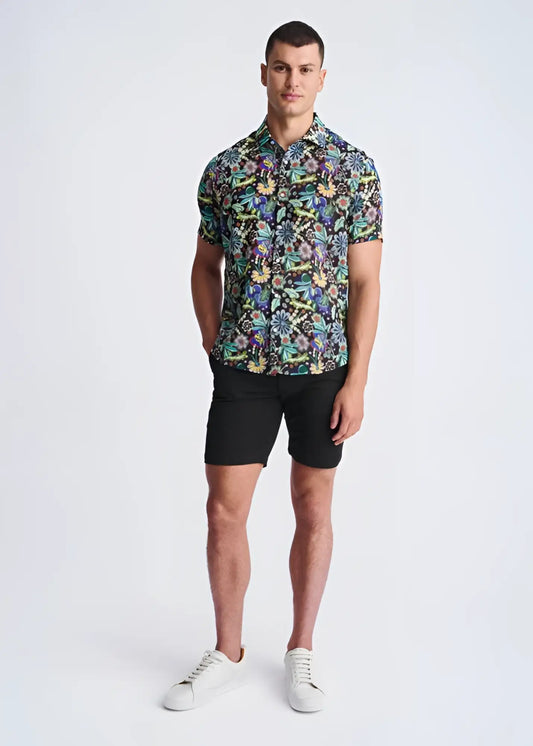 A man wearing a floral lightweight linen tencel short-sleeved shirt with multicolored pattern on a dark background