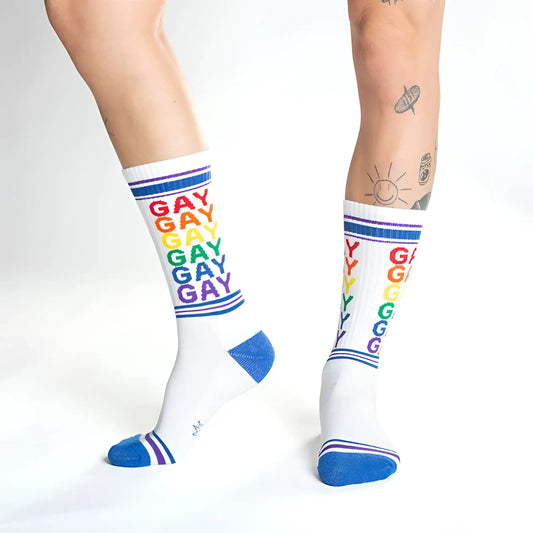 White crew socks with rainbow colored gay text and blue toe heel and cuff accents for pride wear
